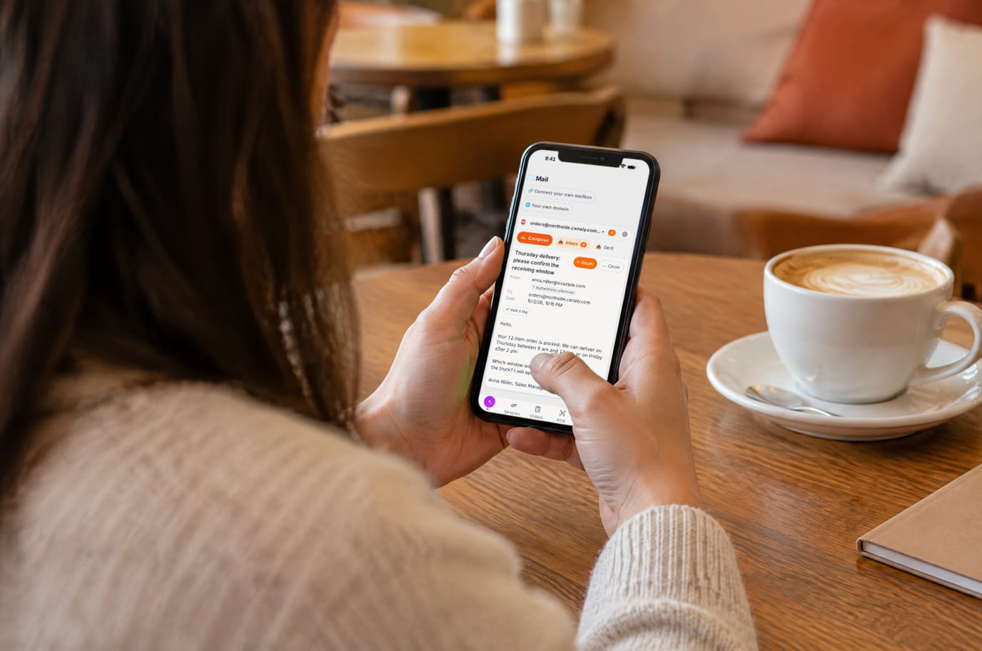 A business owner in a cafe reads a supplier letter in the work mailbox on her phone next to a cappuccino