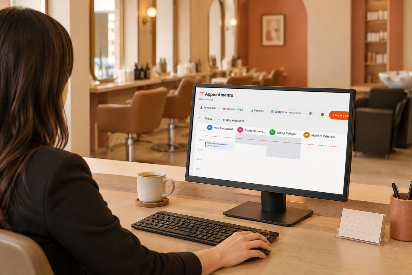 A salon receptionist checks the appointment journal and specialists’ schedules on a monitor